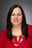 Smiling woman with long dark hair wearing a red blouse and a multi-strand beaded necklace against gray background